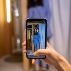 A woman captures an outfit photo with a smartphone in a stylish fitting room.