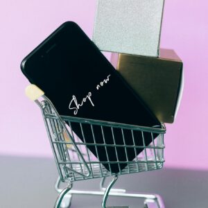 Mini shopping cart with smartphone and gift boxes, symbolizing online shopping.